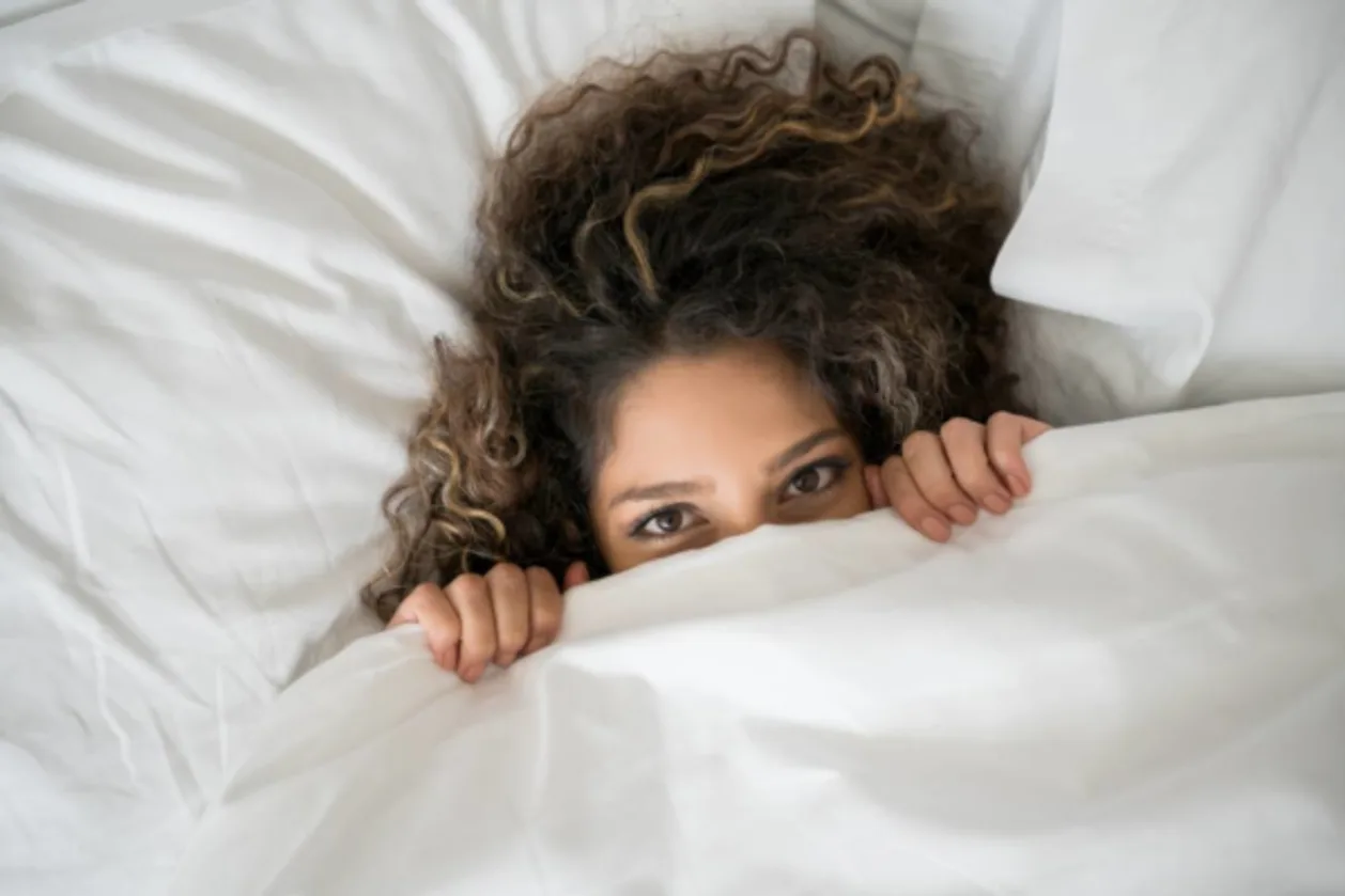 Portrait of a happy woman in bed covering her face with blankets
